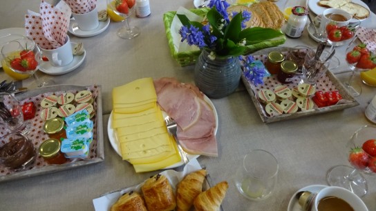 Ontbijttafel met kaas, ham, croissants, jam, boter, aardbeien en bloemen in vaas. (vergroot foto)