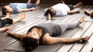 Groep mensen ligt ontspannen op houten vloer in yogastudio, armen en benen gespreid, ogen gesloten. (vergroot foto)
