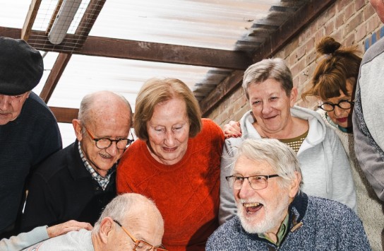 Groep oudere mensen speelt samen jeu de boules en lacht in een overdekte ruimte met bakstenen muur. (vergroot foto)