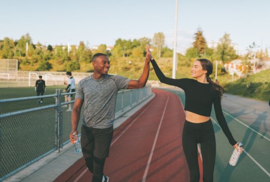 Twee sporters geven elkaar een high five op een atletiekbaan, beiden met een fles water in de hand. (vergroot foto)