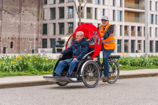 Een man fietst met een oudere man in DE MAX, een driewielige fiets met rode kap. (vergroot foto)