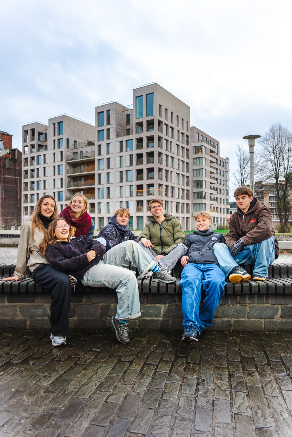 Zes jongeren zitten samen op een bankje buiten, op de Leiedam.
