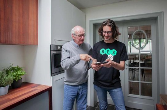 Oudere man en jongere man kijken samen naar een smartphone in een moderne keuken. (vergroot foto)
