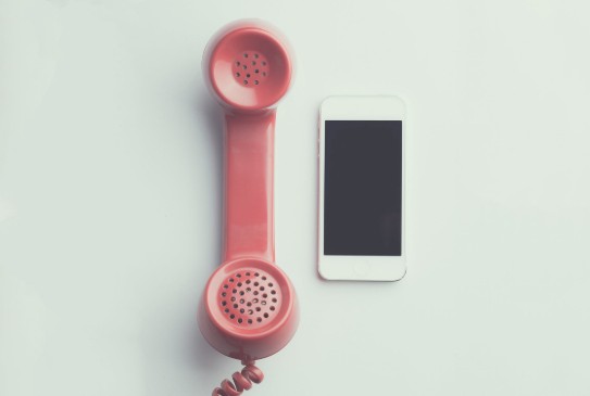 Een roze retro telefoonhoorn naast een moderne witte smartphone op een witte achtergrond. (vergroot foto)