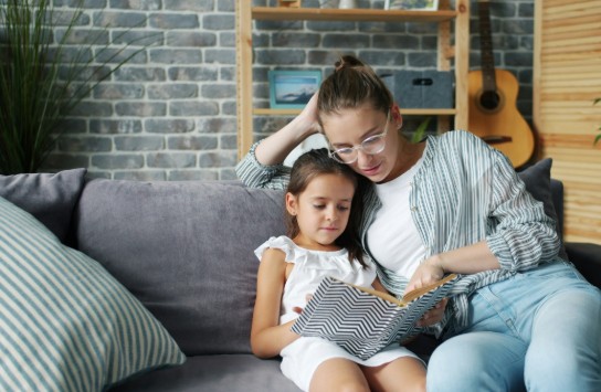 Vrouw leest samen met een meisje een boek op de bank in een gezellige woonkamer. (vergroot foto)