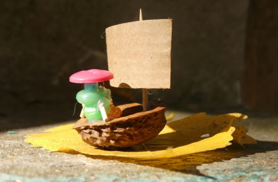 Miniatuurbootje gemaakt van een halve walnoot met een kartonnen zeil en een klein poppetje met roze hoed. (vergroot foto)