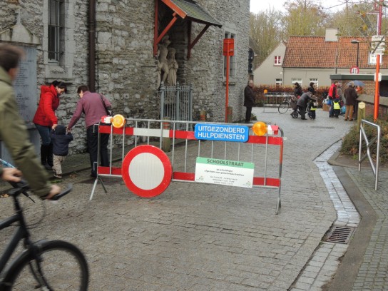 Afzetting met bord "Uitgezonderd hulpdiensten" en mensen met kinderen op een schoolstraat. (vergroot foto)