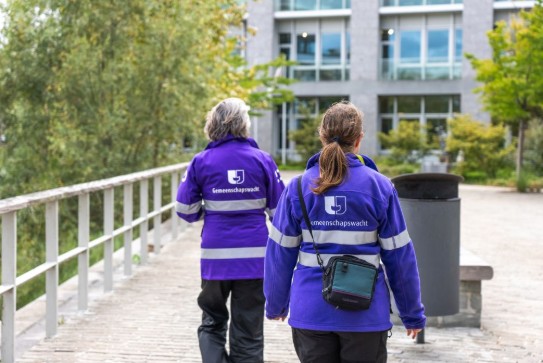 Twee mensen in paarse jassen met 'Gemeenschapswacht' op de rug (vergroot foto)