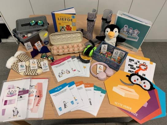 Diverse educatieve materialen met pinguïn-thema, waaronder boeken, kaarten, speelgoed en accessoires op een tafel. (vergroot foto)