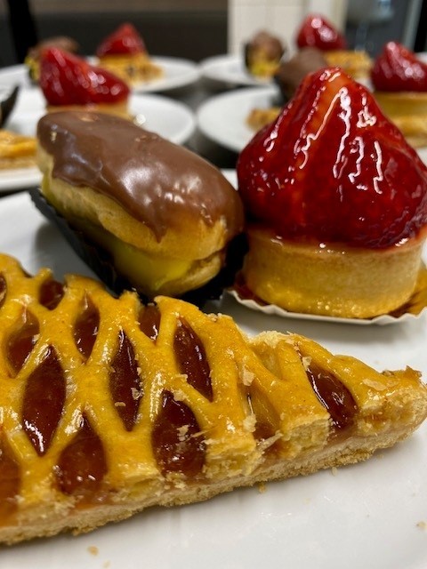 Diverse gebakjes op witte borden, waaronder een aardbeientaartje, chocolade-éclair en een stuk jamtaart. (vergroot foto)