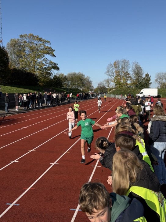 Kinderen rennen op een atletiekbaan terwijl toeschouwers langs de kant juichen en high-fives geven. (vergroot foto)