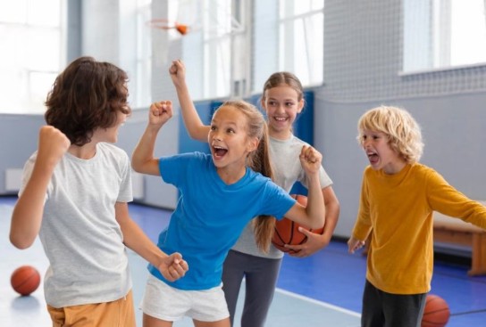 Vier kinderen vieren een overwinning in een gymzaal met basketbal, blij en enthousiast. (vergroot foto)